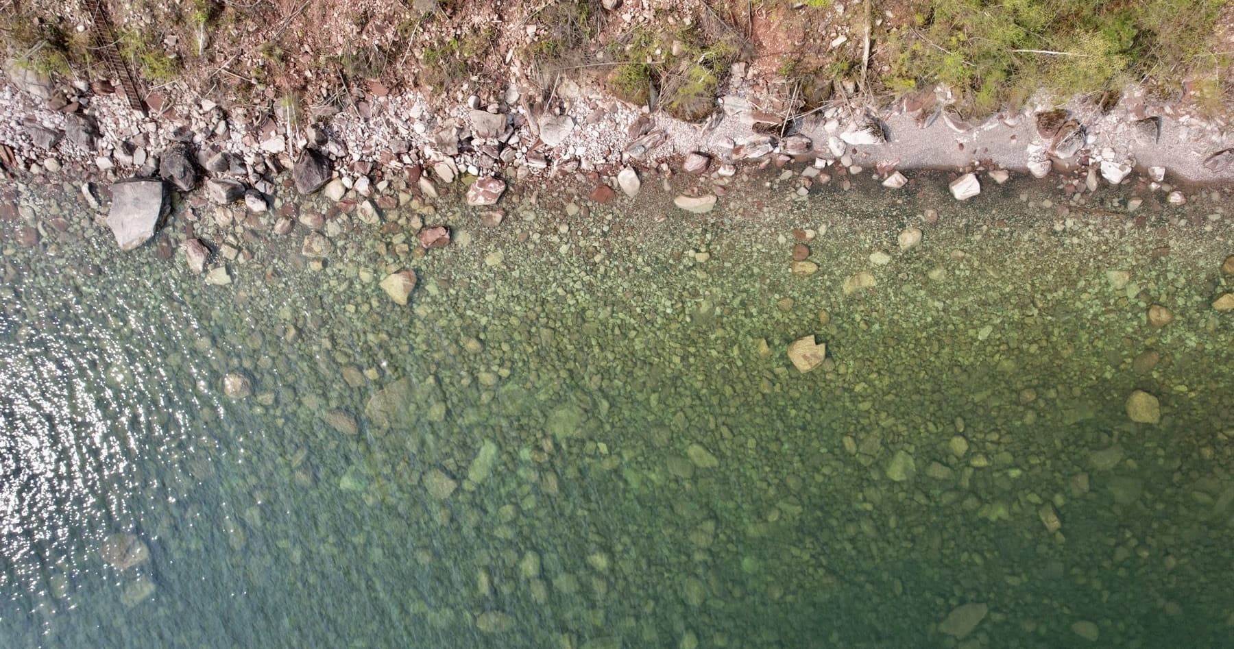 Overhead view of clear Lake Superior water over rounded cobbles at the foot of a red sandstone bank.