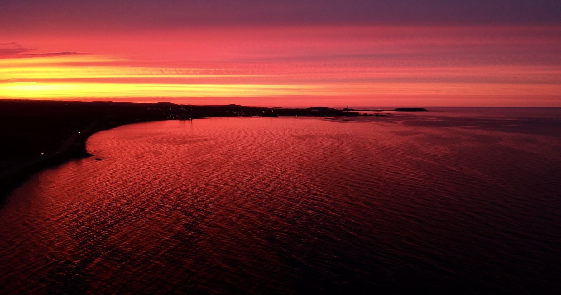 Lake Superior glowing red and orange beneath a dramatic sunset sky over the shoreline.